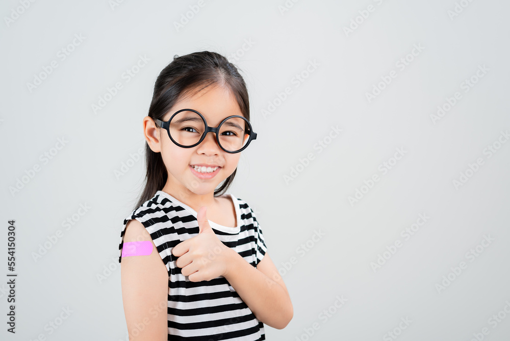 Asian little girl wear glasses showing her arm with bandage after virus vaccine happy Kid and child vaccination campaign. Protect your kid with vaccine concept Asian little girl wear glasses showing her arm with bandage after virus vaccine happy Kid and child vaccination campaign. Protect your kid with vaccine concept