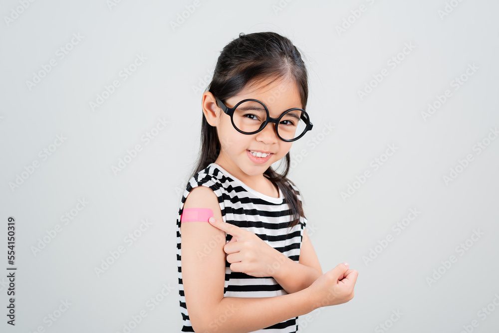 Asian little girl wear glasses showing her arm with bandage after virus vaccine happy Kid and child vaccination campaign. Protect your kid with vaccine concept Asian little girl wear glasses showing her arm with bandage after virus vaccine happy Kid and child vaccination campaign. Protect your kid with vaccine concept