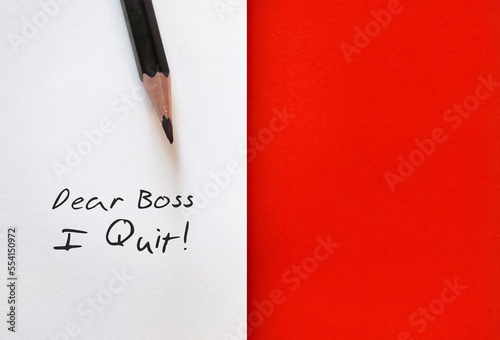 Pencil on white paper with handwritten text DEAR BOSS I QUIT, on red copy space background, concept of decision making to quit job, employees resign from full time job in the great resignation trend 