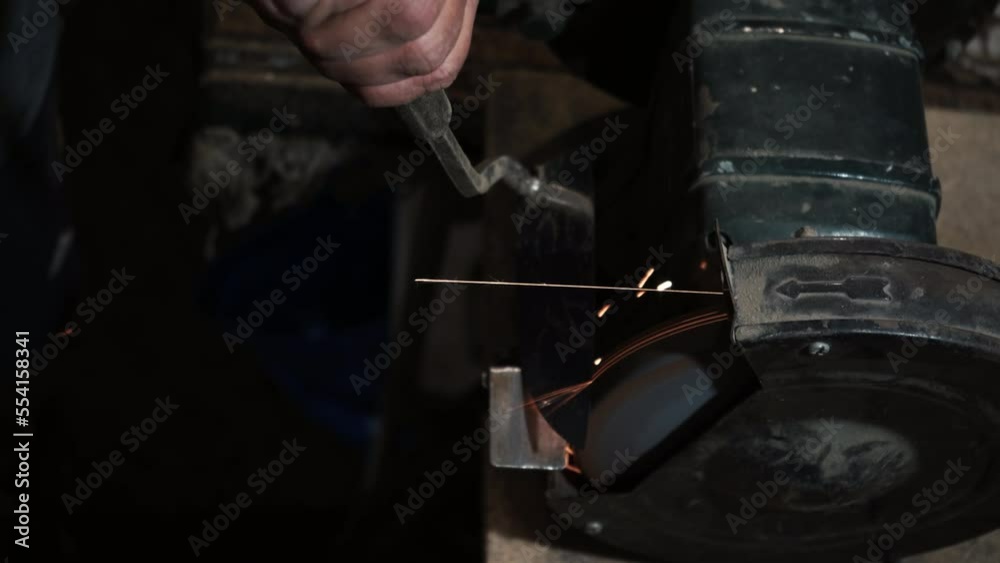 Sharpening a knife on an electric grinding wheel, Machine sharpening a scabbard on an electric grinder, manual sharpening on a rotating grinding stone, close-up. Sharpening a knife on an electric grinding wheel, Machine sharpening a scabbard on an electric grinder, manual sharpening on a rotating grinding stone, close-up.