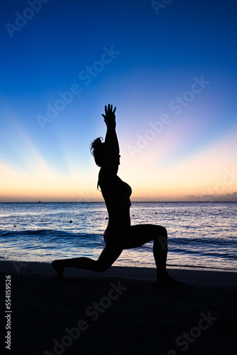 Woman doing a yoga pose in silhouette in front of a sunset - Caribbean ocean - wellness vibes