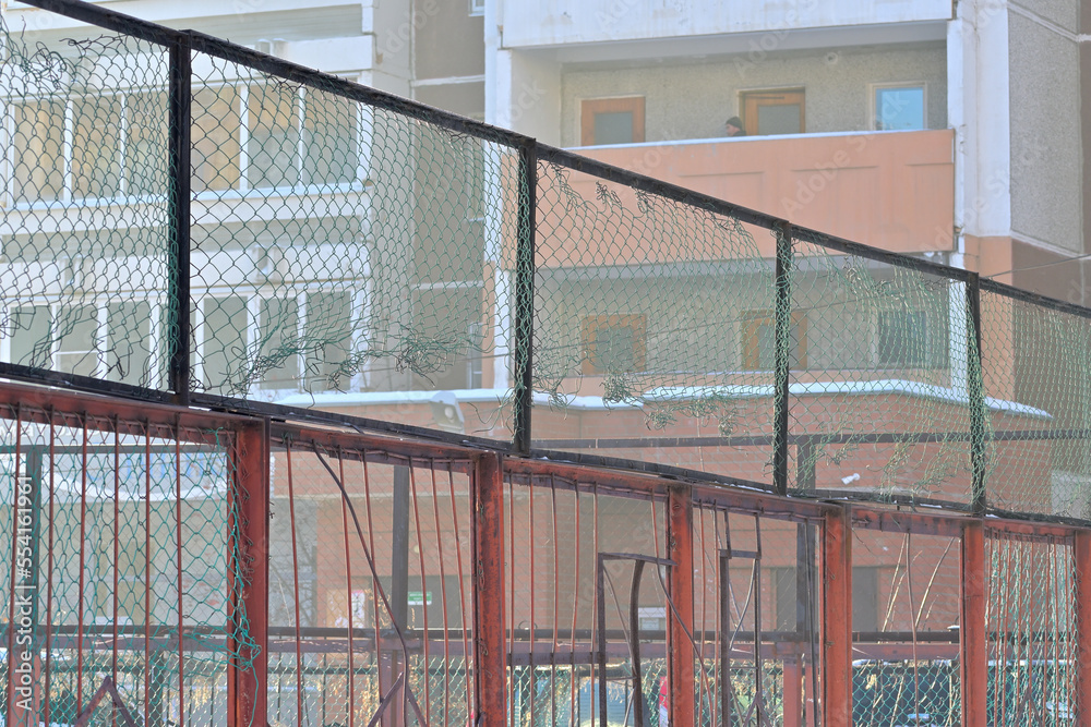 Metal fencing of a sports ground in the courtyard of a multi-storey residential building on a winter day
