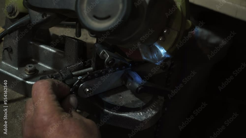 A man at work sharpening the metal chain with the grinder in an industrial environment. Close-up. A man at work sharpening the metal chain with the grinder in an industrial environment. Close-up.