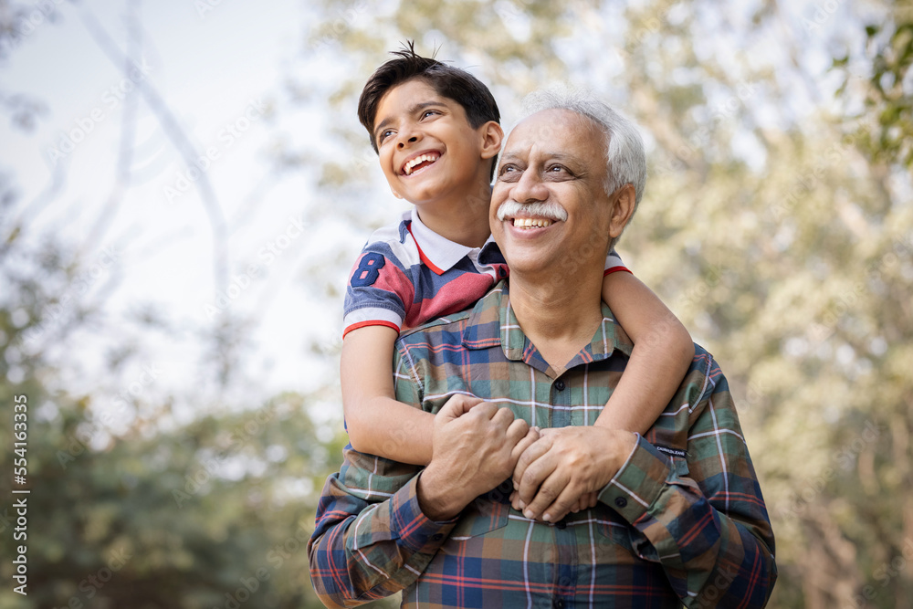 Naklejka premium Senior man piggybacking grandson in park during weekend.