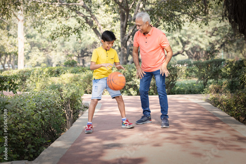 Grandfather and grandson playing basketball at park.