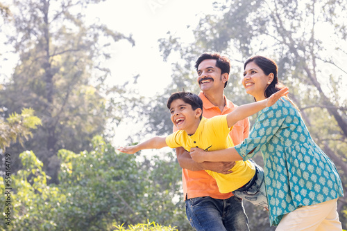 Cheerful parents assisting son in flying at park.
