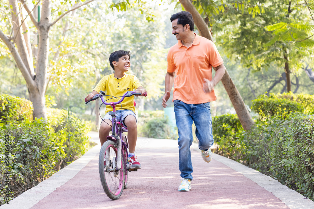 Boy learning bicycle with assistance of father at park Boy learning bicycle with assistance of father at park