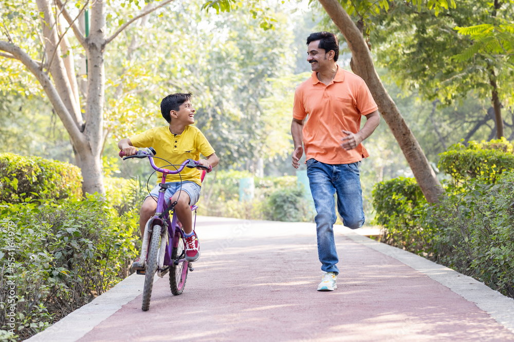Boy learning bicycle with assistance of father at park Boy learning bicycle with assistance of father at park