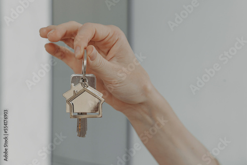 Woman holding house shaped keychain, selective focuse on female hand with key from new home