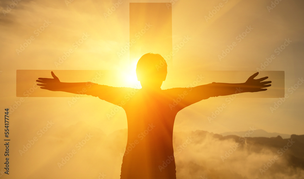 The boy stood with his arms outstretched, with a cross in front of him and sky light.