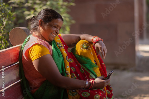 A house maid sitting in the colony park using her mobile phone during her resting period  photo