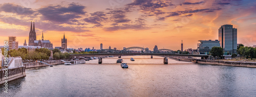 Panoramic view of the city of Koln, the Rhine River, bridges and various barges and ships during majestic sunset.