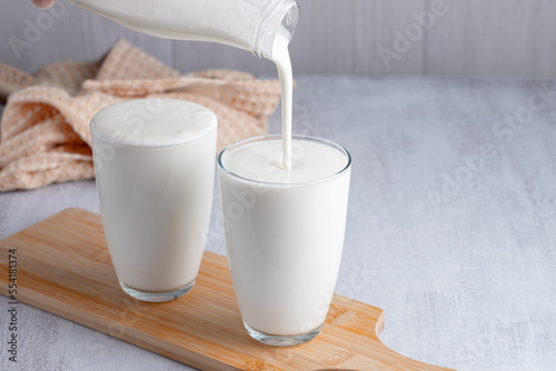 Pouring homemade kefir, buttermilk or yogurt with probiotics. Yogurt flowing from glass bottle on light background. Probiotic cold fermented dairy drink. Trendy food and drink. Copy space