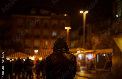Rear view of adult man with hood on street at night