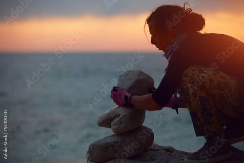 Silhouette of a woman balancing rocks and stones on the ocean sea coast at sunset sunrise time.