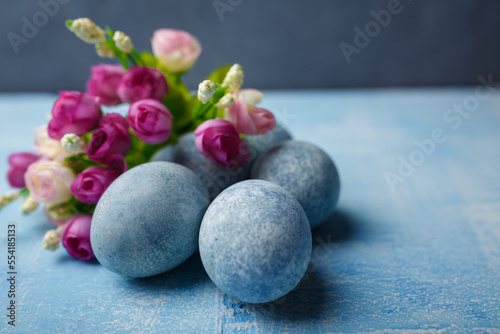 Painted Easter eggs on blue background with purple flowers. Spring holiday, symbolic food. Close up shot, copy space.