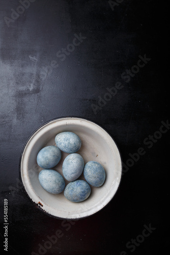 Easter eggs painted blue in white bowl on black wooden background. Top view, copy space, vertical shot