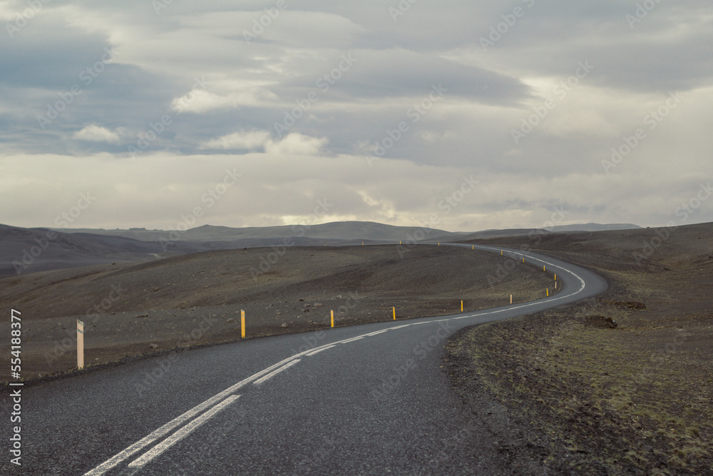 Empty road across hills landscape photo. Beautiful nature scenery photography with cloudy sky on background. Idyllic scene. High quality picture for wallpaper, travel blog, magazine, article