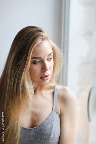 Caucasian young woman natural blonde with long hair and large silicone lips. Close-up portrait at window.