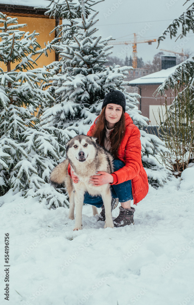 girl and her cute alaskan malamute dog playing outdoors in the snow. Winter holidays concept