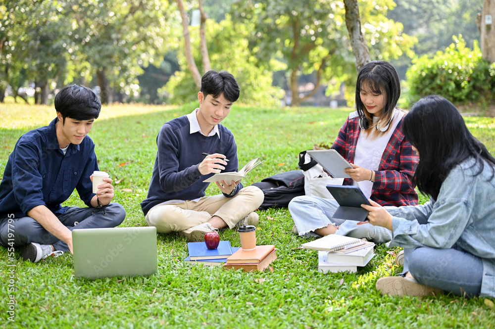 Happy young Asian college students relaxing in the campus's park, working their group project Happy young Asian college students relaxing in the campus's park, working their group project