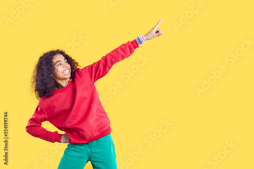 Funny biracial teen girl isolated on yellow studio background point up at good sale or promotion offer. Happy African American teenager show deal. Copy space and advertising placement.