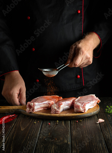 Professional chef adds paprika to raw meat ribs before grilling. Work environment on the kitchen table with spices and condiments