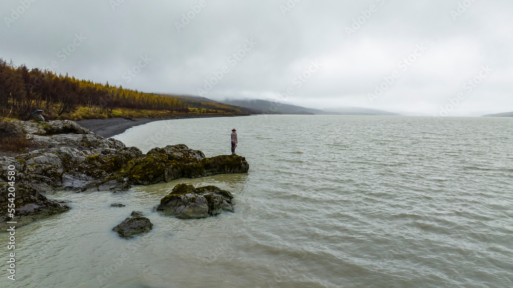 young woman on the rock at river with spruce pine forrest on the coast young woman on the rock at river with spruce pine forrest on the coast
