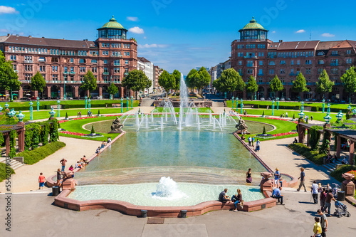 Beautiful view of the cascade water fountain behind the famous Water Tower (Wasserturm) in the square Friedrichsplatz in Mannheim, Germany. The water runs into a large water basin with a fountain.