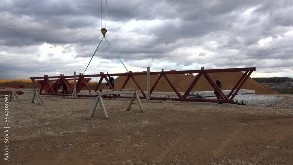 Workers are mounting of the beam frame (metal structure) on the lifting crane hook at a construction site. Workers are mounting of the beam frame (metal structure) on the lifting crane hook at a construction site.