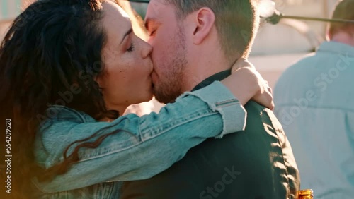 Dance, party and couple kiss, happy and smile while dancing with a crowd on a rooftop, in love and cheerful. Music, love and woman with man at festival kissing, flirt and and enjoy social event