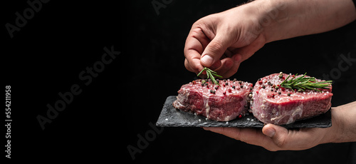 Preparing fresh beef or pork on a dark background. Chef salts steak in a freeze motion with rosemary and spices. Long banner format. photo