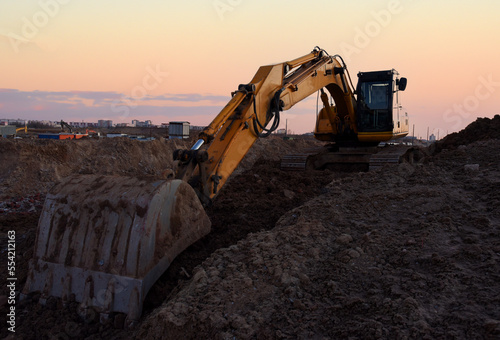 Excavator working on earthmoving at open pit mining on amazing sunset background. Backhoe digs sand and gravel in quarry. Heavy construction equipment during excavation at construction site