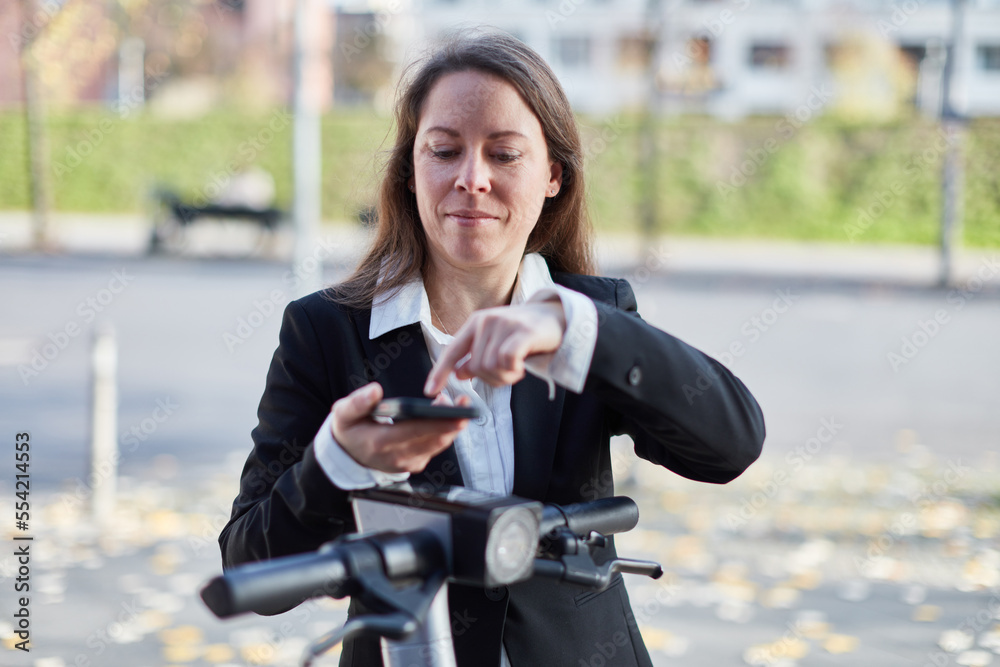 Smiling businesswoman using smartphone app to rent e-scooter Smiling businesswoman using smartphone app to rent e-scooter