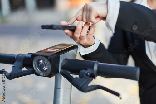 Hand of businesswoman renting e-scooter with smartphone