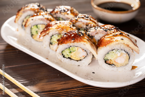 Sushi roll with eel and shrimp on plate on wooden background.