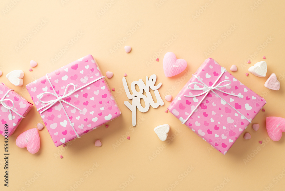 Valentine's Day concept. Top view photo of pink gift boxes inscription love you heart shaped marshmallow candles and sprinkles on isolated beige background Valentine's Day concept. Top view photo of pink gift boxes inscription love you heart shaped marshmallow candles and sprinkles on isolated beige background