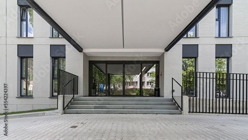 Wejście do obiektu biurowego. Elewacja wykonana z tynku i akcentami betonu. Harmonijny i spójny układ okien.