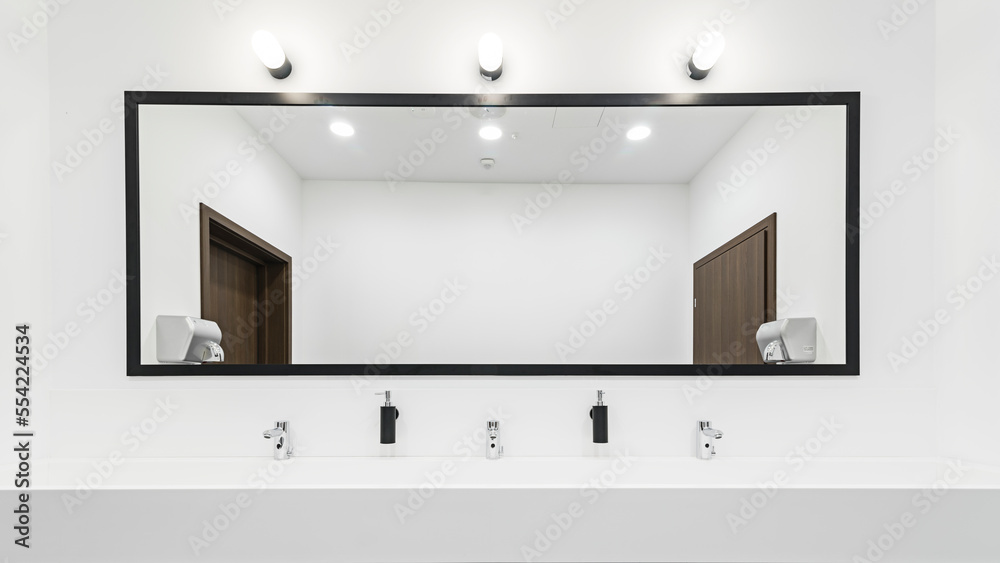 Nowoczesna toaleta z dużym oświetlonym lustrem. Szeroka umywalka z kranami na kilka osób. Jasna i przestronna łazienka. - obrazy, fototapety, plakaty 