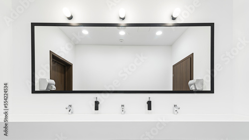 Nowoczesna toaleta z dużym oświetlonym lustrem. Szeroka umywalka z kranami na kilka osób. Jasna i przestronna łazienka.