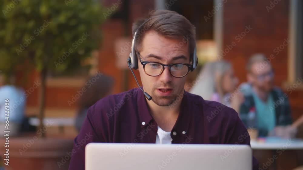 Attractive young man in headset having a video call on laptop sitting in the cafe. Realtime Attractive young man in headset having a video call on laptop sitting in the cafe. Realtime