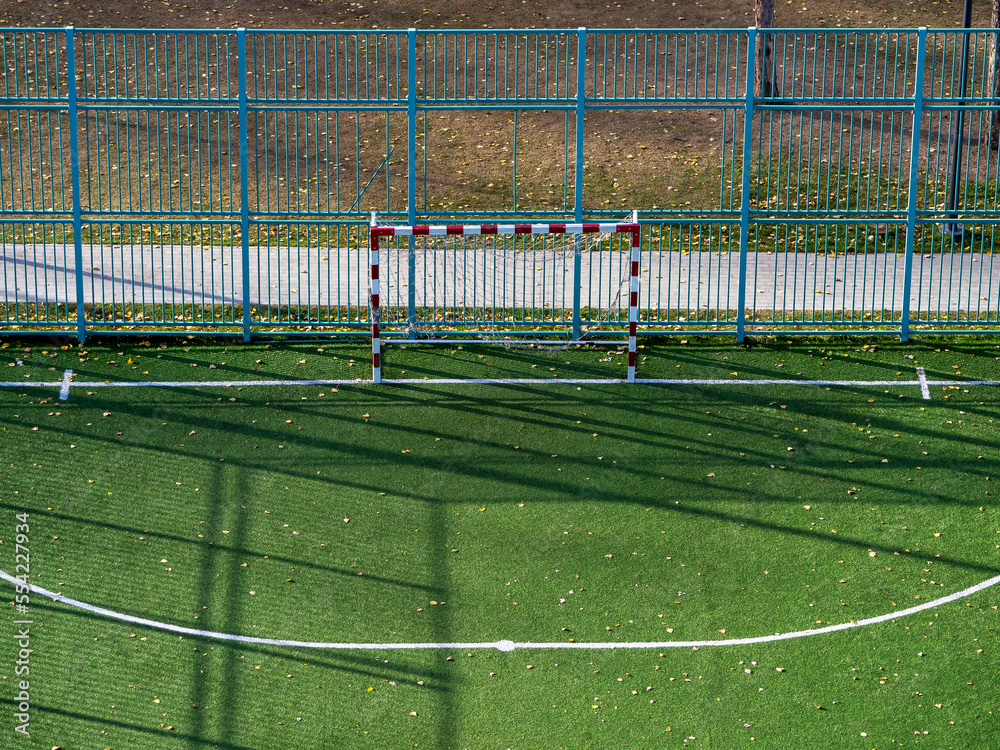 Obraz premium The football field, markings and fences are illuminated by the sun. Frontal view of the football goal from above.