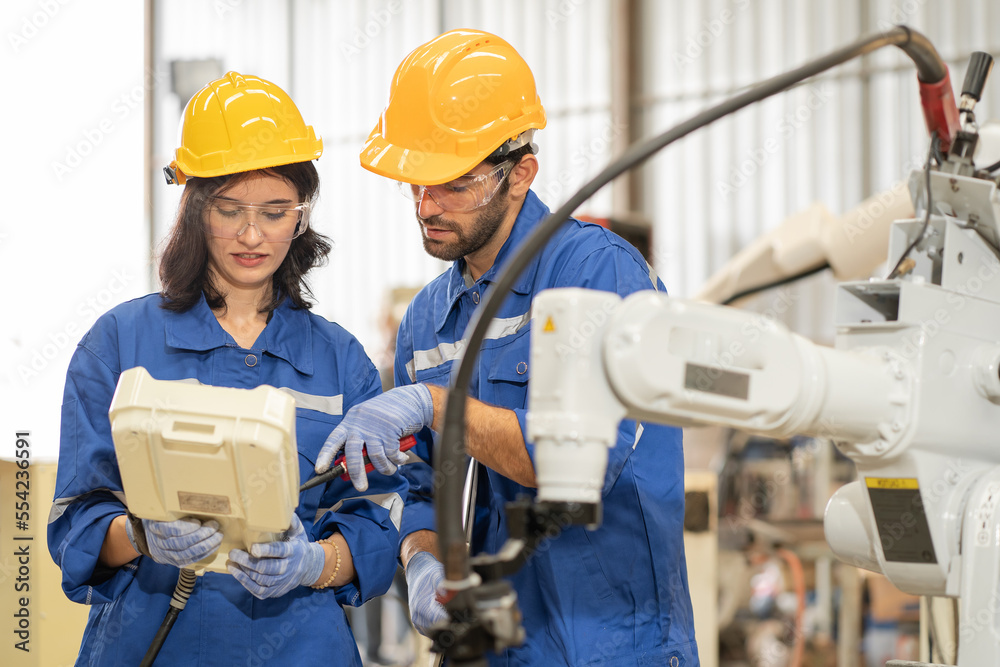 Female industrial engineer using remote control board to check robotic welder operation in modern automation factory. Technician man monitoring robot controller system for automated steel welding. Female industrial engineer using remote control board to check robotic welder operation in modern automation factory. Technician man monitoring robot controller system for automated steel welding.