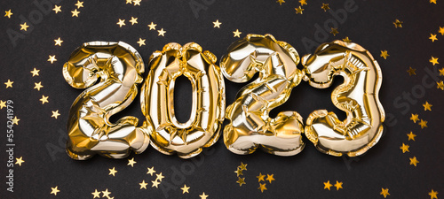 New year 2023 balloon celebration card. Gold foil helium balloon number 2023 and gold confetti stars isolated on black background. Flat lay, merry christmas, happy holidays mockup.