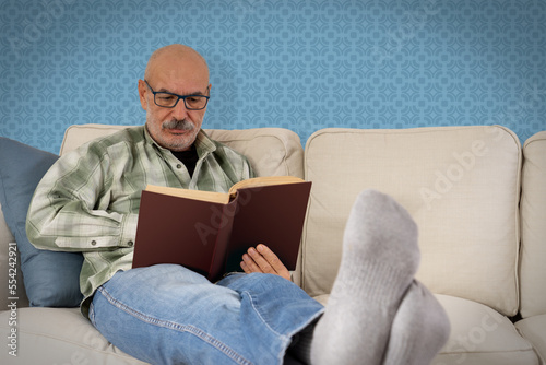 Happy Senior Man Sitting on Sofa and Reading Book at Home