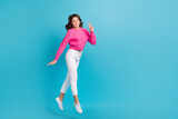 Full length photo of shinny friendly lady wear pink walking showing v-sign empty space jumping high isolated blue color background