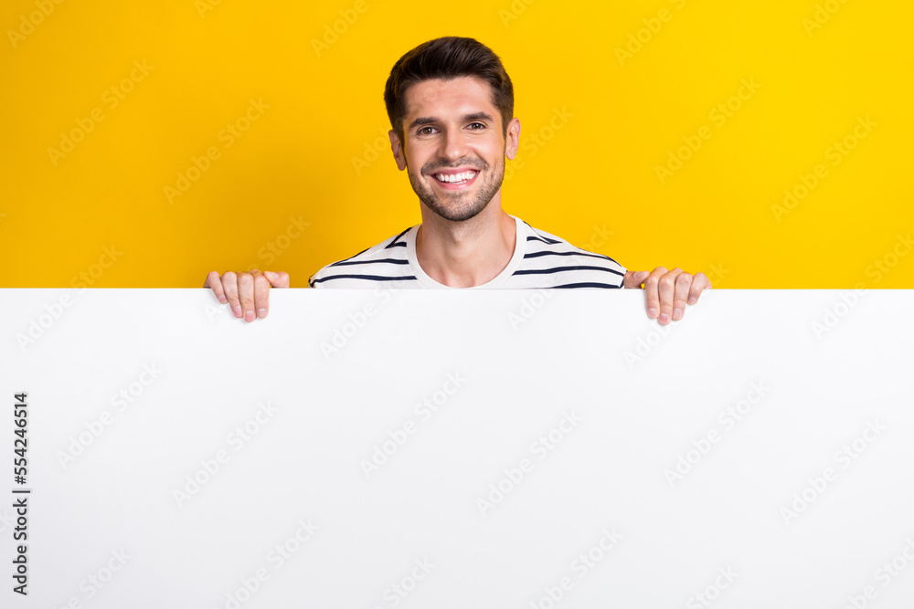 Photo of good mood pretty guy dressed striped t-shirt holding hands arms empty space isolated yellow color background Photo of good mood pretty guy dressed striped t-shirt holding hands arms empty space isolated yellow color background