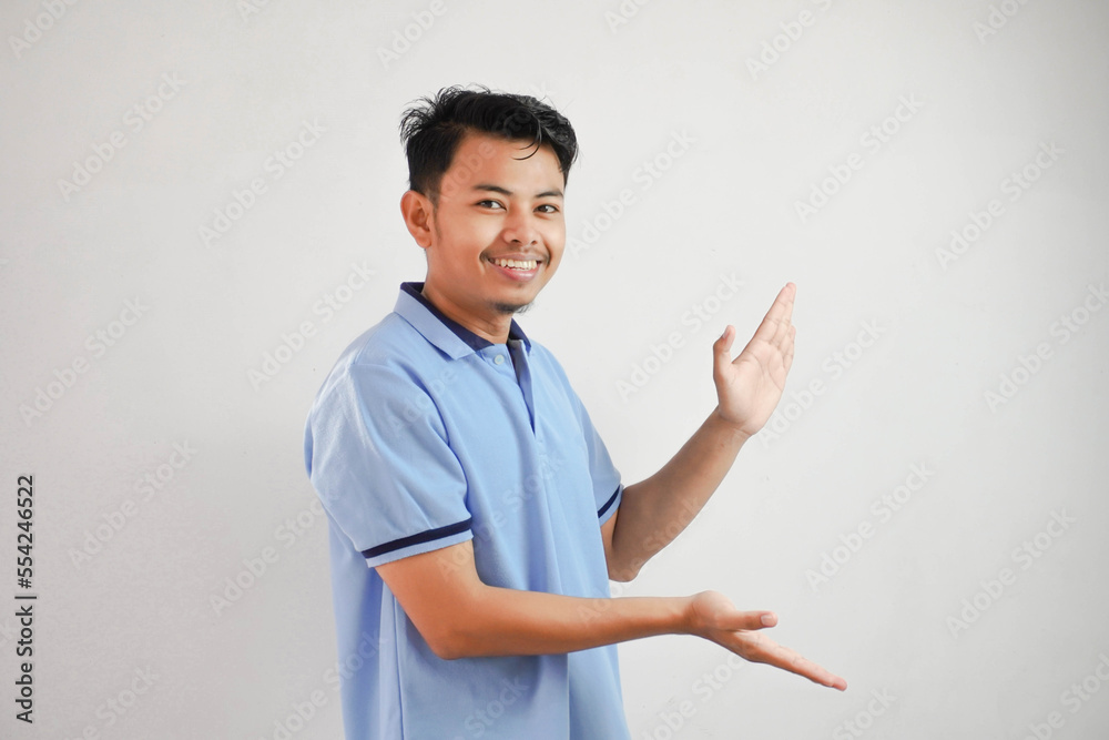 smiling asian man open arms pointing to the sides wearing blue t shirt isolated on white background smiling asian man open arms pointing to the sides wearing blue t shirt isolated on white background