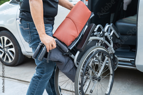 Asian woman folding and lift up wheelchair into her car. Accessibility concept.