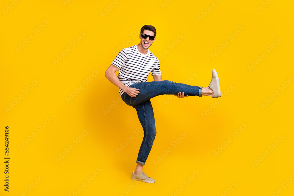 Full length photo of excited cool man wear white t-shirt dark glasses playing leg guitar having fun isolated yellow color background Full length photo of excited cool man wear white t-shirt dark glasses playing leg guitar having fun isolated yellow color background
